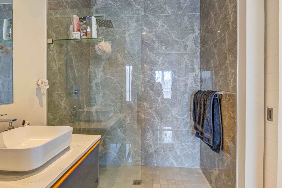 Modern bathroom featuring a walk-in shower with grey marble-effect wall tiles, a glass shower screen, and a contemporary vessel sink vanity.