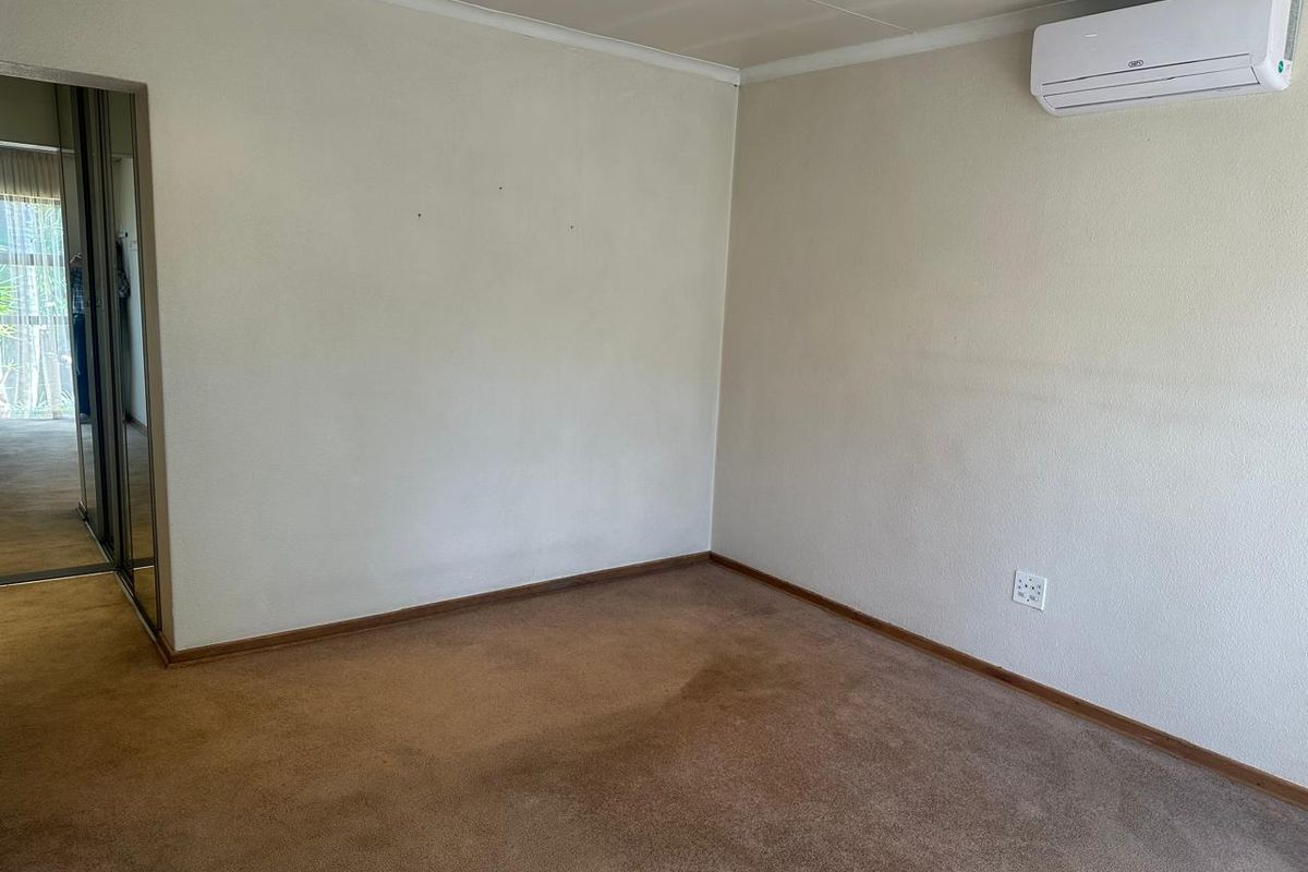 An empty bedroom featuring neutral walls, carpeted flooring, a wall-mounted air conditioning unit, and a doorway leading to a closet area.