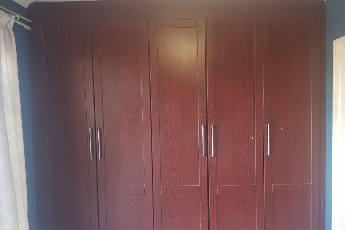 A bedroom featuring built-in floor-to-ceiling wooden wardrobes with modern metal handles.
