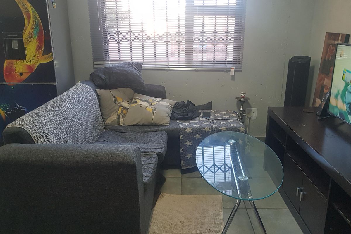 A compact living room featuring tiled flooring and a window fitted with horizontal blinds and security bars.