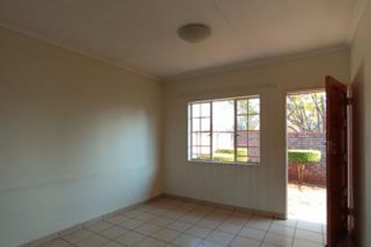 An empty bedroom featuring tiled flooring, a grid-pattern window, and direct access to an outdoor area through a wooden door.