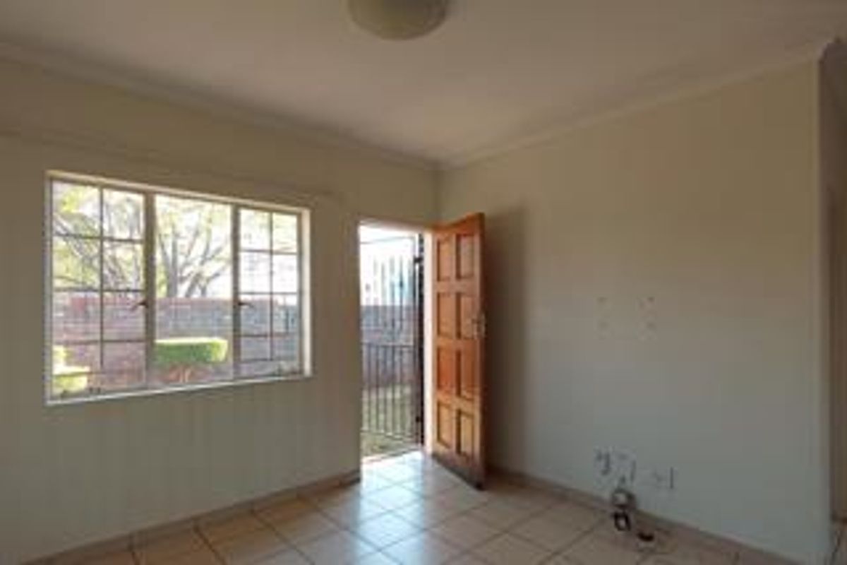 An empty living room featuring tiled flooring, a timber door leading to the exterior, and a window with security bars.