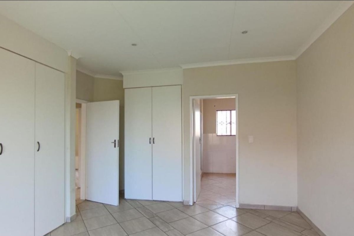 A bright bedroom featuring built-in cupboards, tiled flooring, and direct access to an adjoining room.