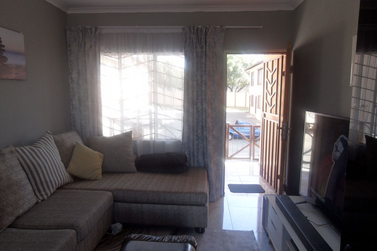 A living room area featuring tiled flooring and a security gate at the entrance, providing direct access to the exterior.