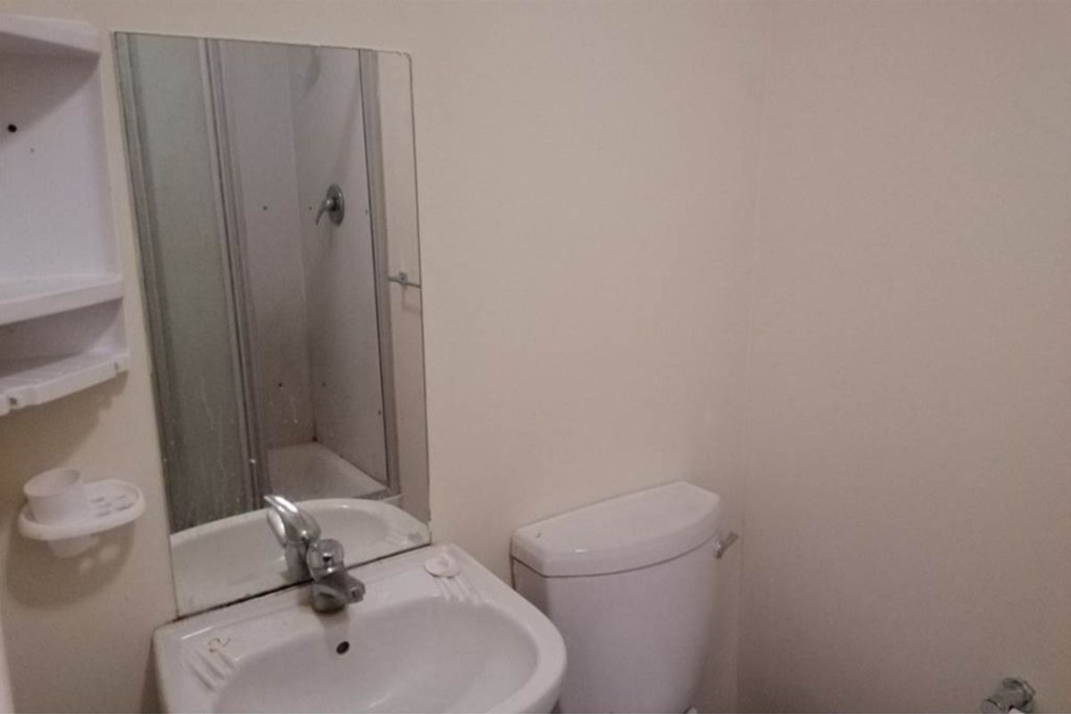 A functional bathroom featuring a standard toilet, pedestal basin with chrome faucet, wall-mounted mirror, and a shower enclosure.