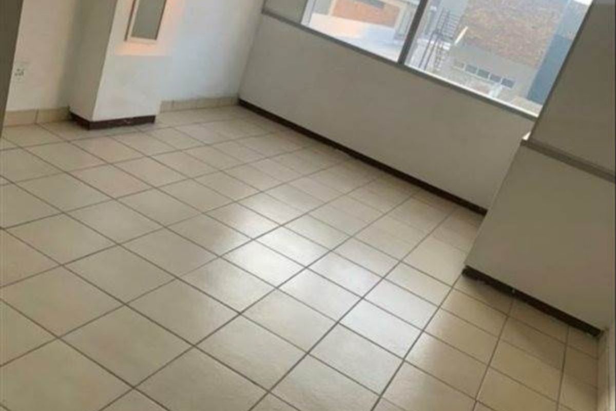 An empty, tiled living area featuring large windows that provide natural light and a view of the surrounding exterior.