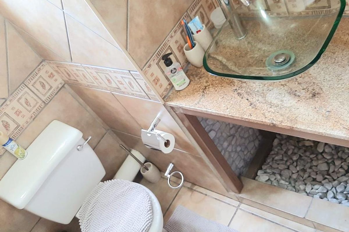 Compact bathroom featuring a glass vessel sink on a stone-topped vanity with decorative wall tiling and a standard toilet.