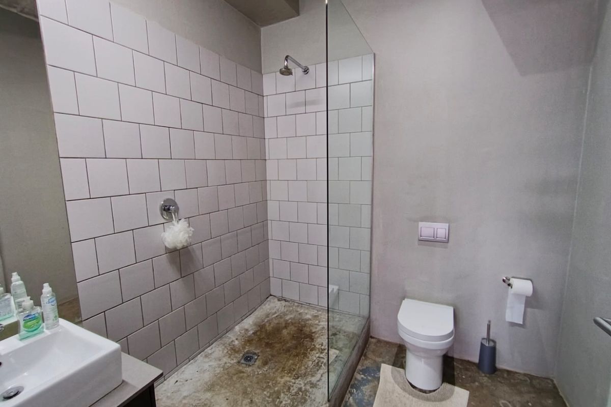 A bathroom featuring a walk-in shower with subway tile surround, a wall-mounted toilet, and a vanity basin, requiring significant maintenance and floor restoration.