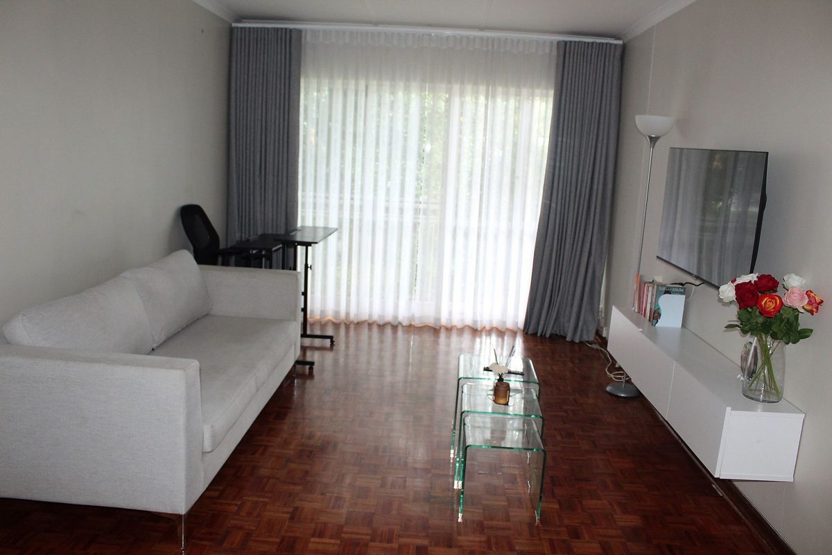 A living room featuring polished parquet flooring, floor-to-ceiling curtains, and a wall-mounted television unit.