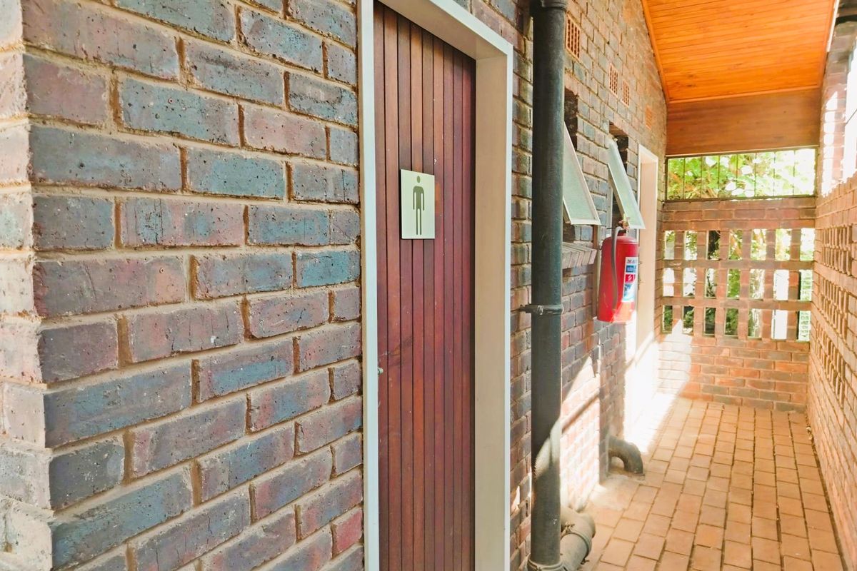 Exterior corridor featuring exposed brick walls, timber ceiling, and access to communal restroom facilities.
