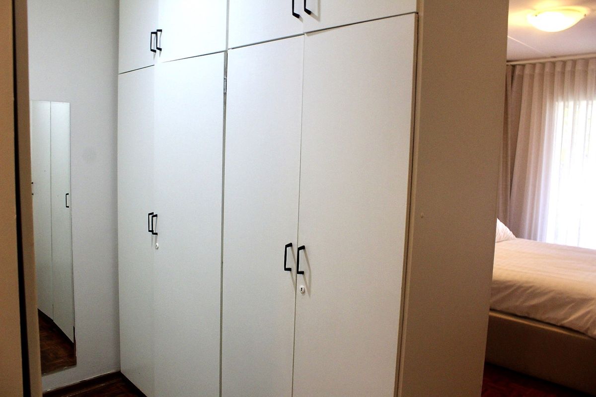 A bedroom featuring built-in floor-to-ceiling white cabinetry with modern black handles and an integrated full-length mirror.