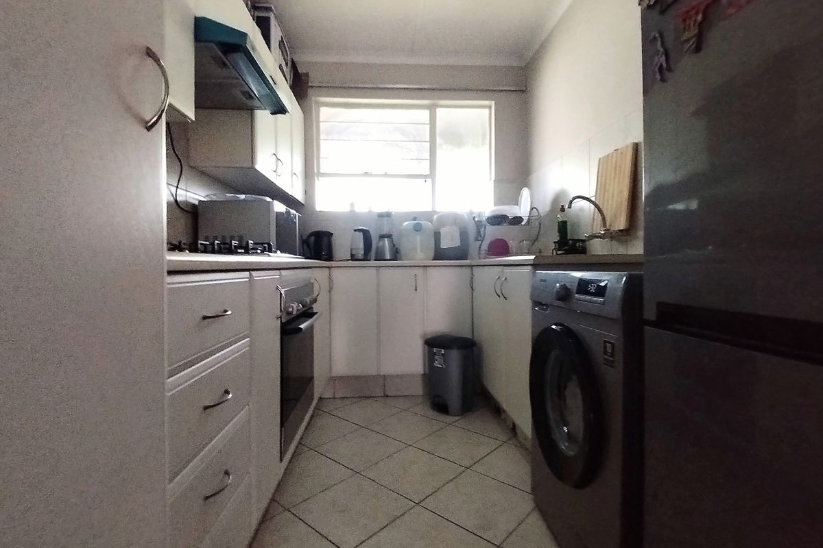 A compact galley-style kitchen featuring white cabinetry, tiled flooring, a built-in oven, and a dedicated space for laundry appliances.