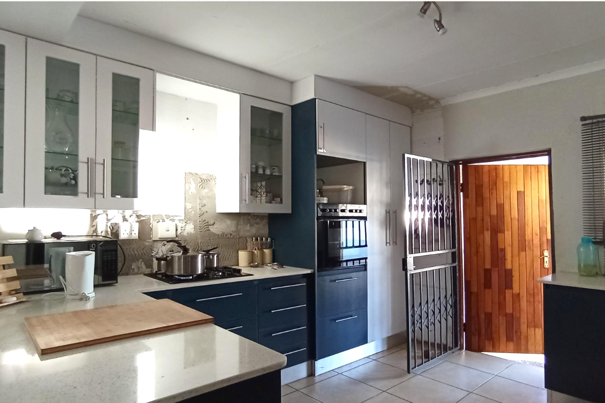 Modern kitchen featuring two-tone cabinetry, stone countertops, built-in oven, and gas hob, with direct access to an exterior door.