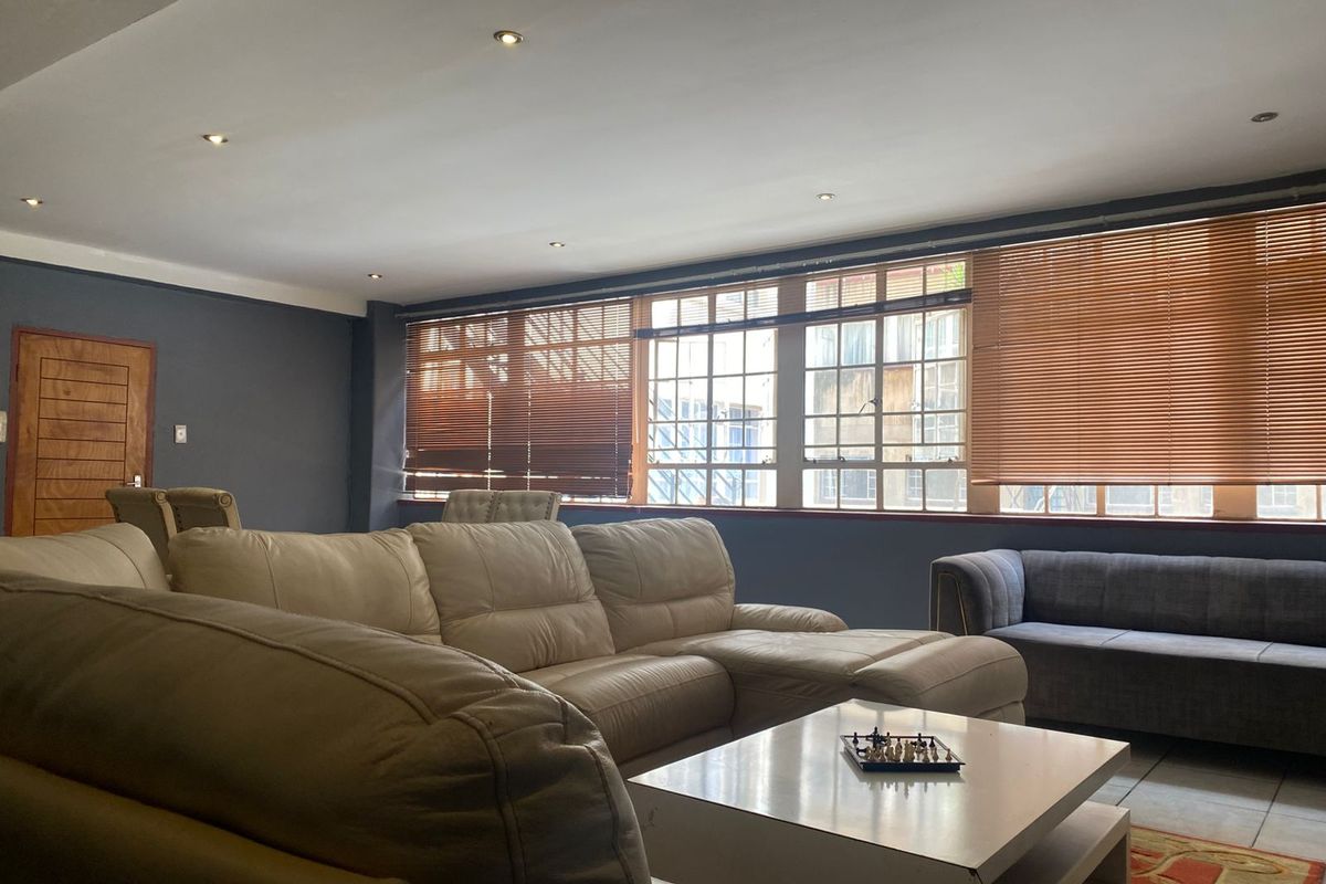 Spacious living room featuring large windows with fitted wooden blinds, recessed ceiling lighting, and tiled flooring.