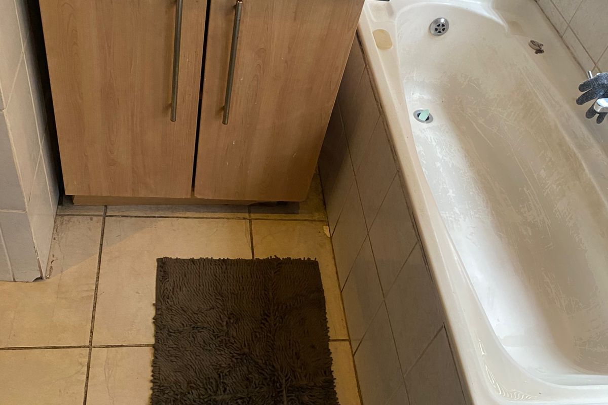 A functional bathroom featuring a built-in bathtub with tiled surround and a vanity cabinet with a countertop basin.