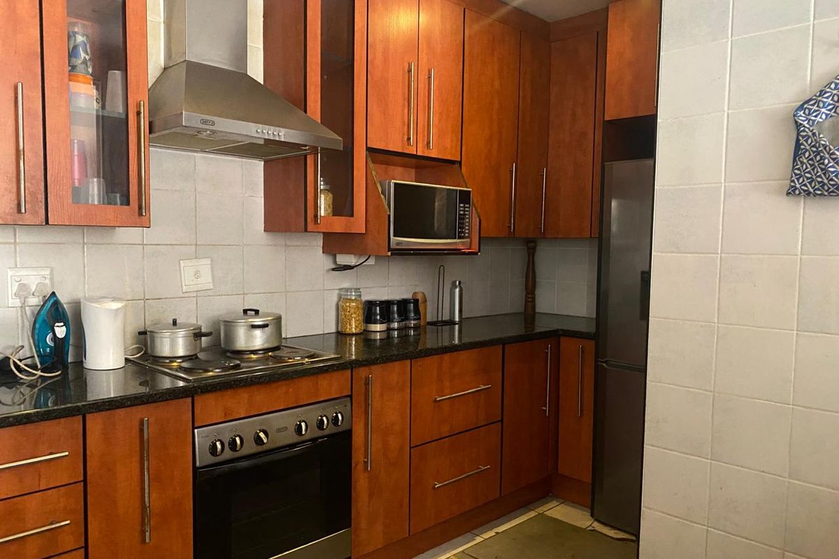 A functional kitchen featuring wooden cabinetry, granite countertops, a built-in oven, hob, and stainless steel extractor fan.