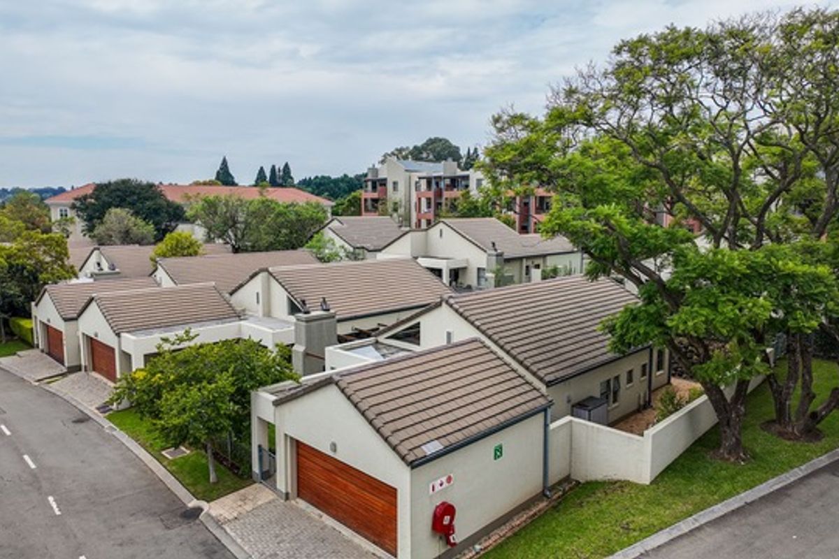 Aerial view of a residential apartment complex featuring tiled roofs, paved driveways, and established trees within a well-maintained estate setting.