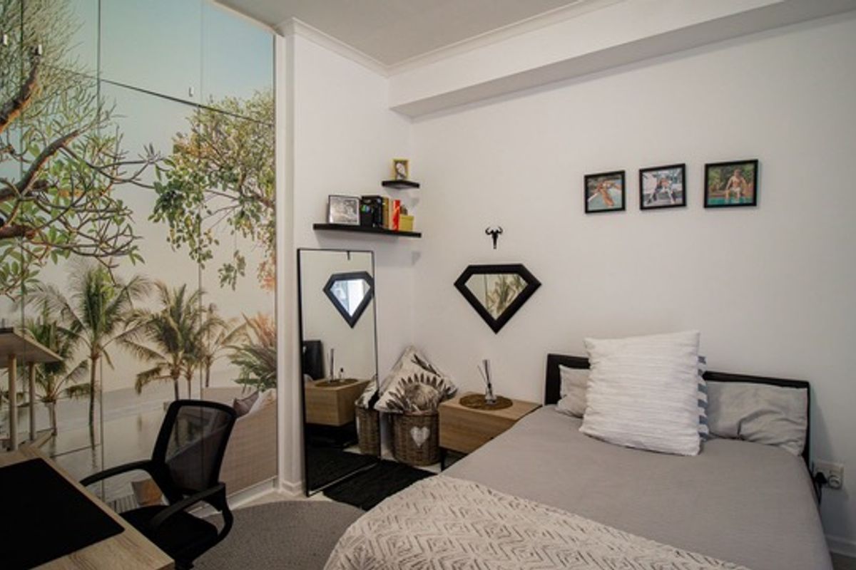 A well-maintained bedroom featuring a large floor-to-ceiling mural wardrobe, neutral walls, and ample space for a double bed.