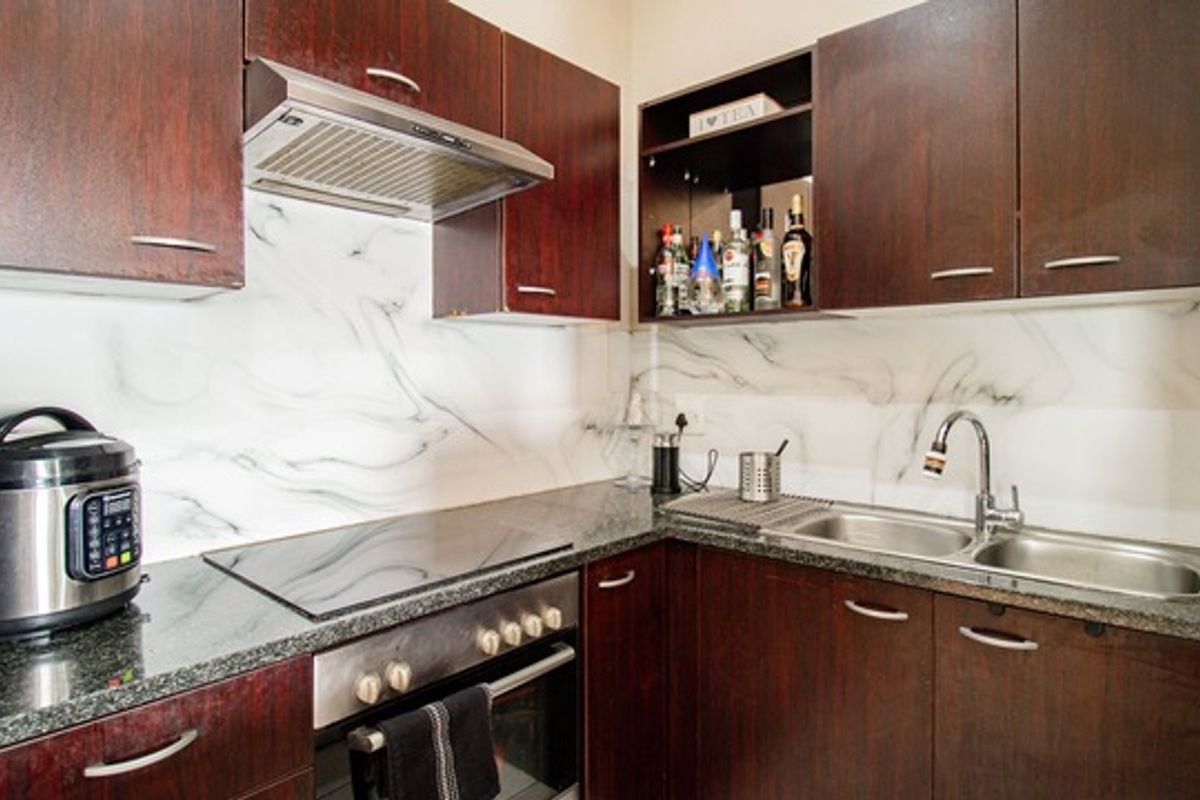 A compact kitchen featuring dark wood cabinetry, a built-in oven with a glass cooktop, an extractor fan, and a modern marble-effect splashback.