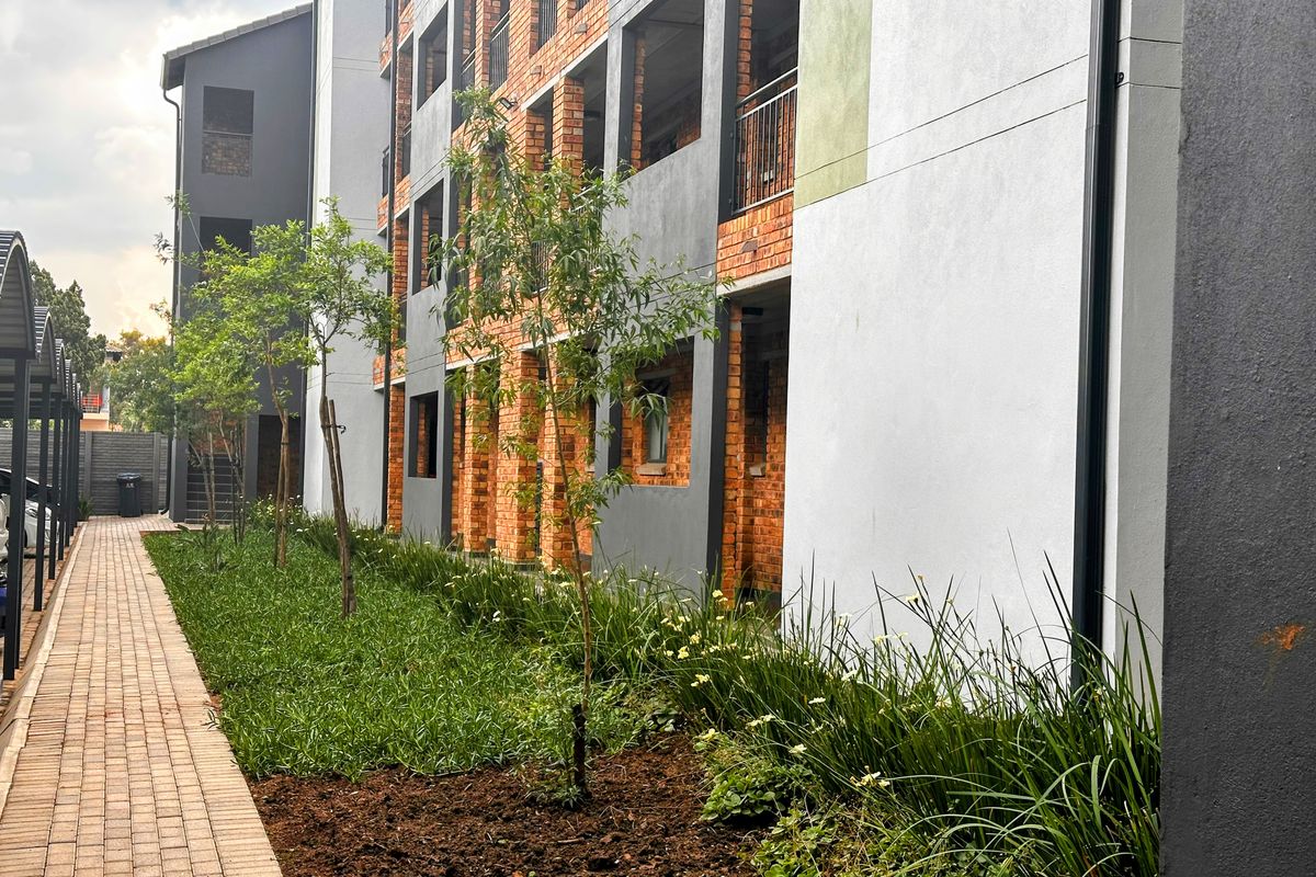 Exterior view of a modern townhouse complex featuring brick and rendered facade, paved walkway, and landscaped garden beds.