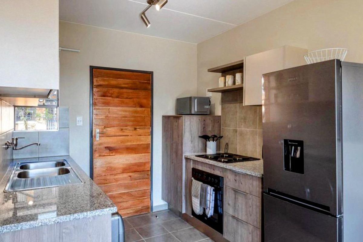 Compact kitchen featuring granite countertops, built-in oven, gas hob, stainless steel sink, and wood-finish cabinetry.