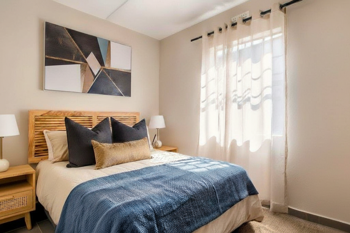 A well-lit bedroom featuring neutral wall tones, a window with sheer curtains, and tiled flooring.