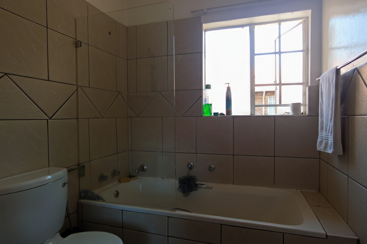 A functional bathroom featuring a built-in bathtub with a glass shower screen, tiled walls, and a window providing natural light.