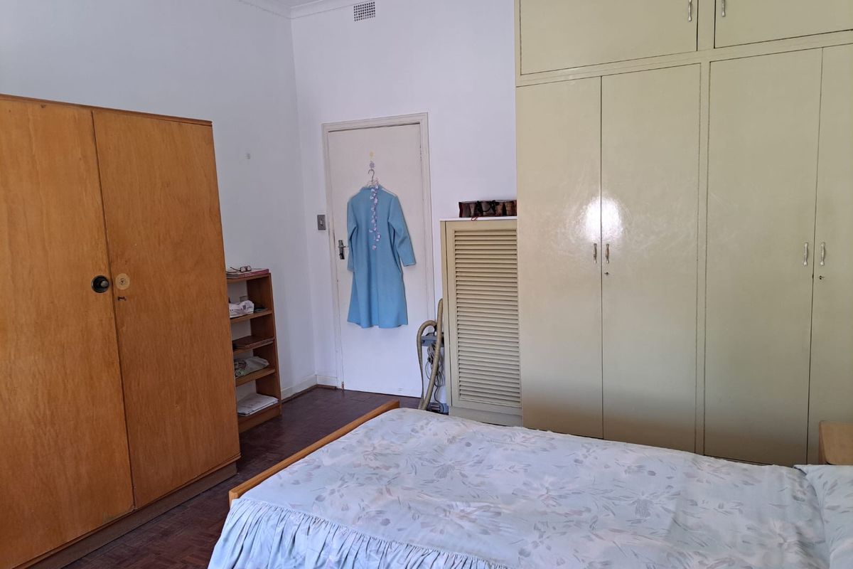A bedroom featuring built-in cupboards, parquet flooring, and a neutral color palette, offering a functional space with potential for modernization.