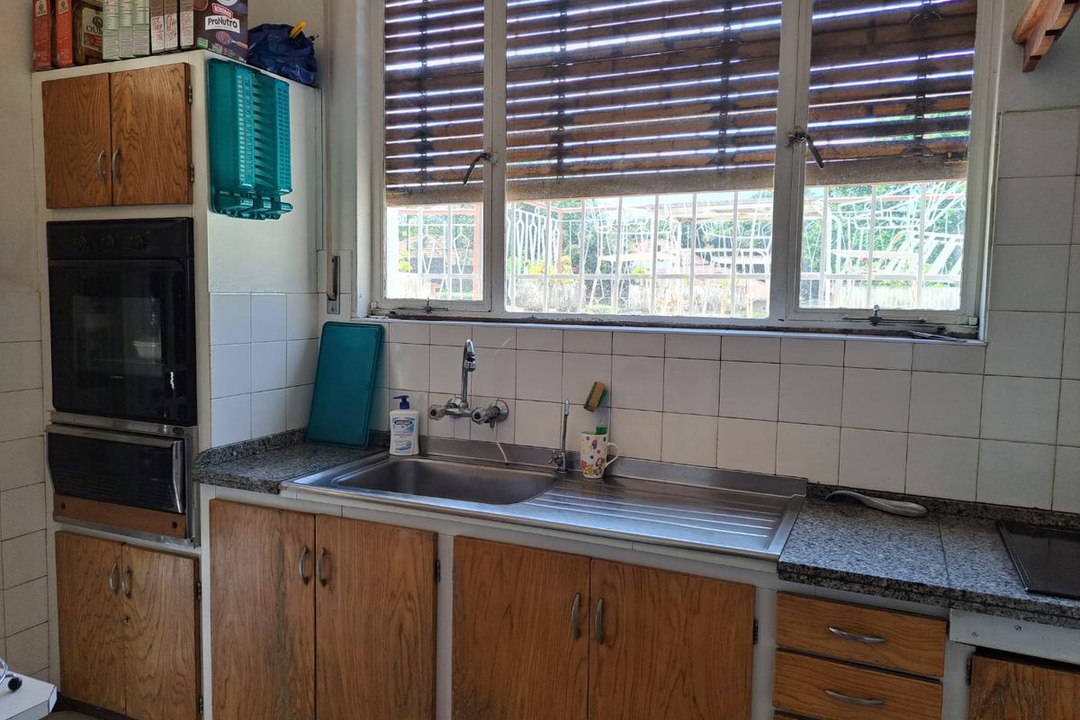 A dated kitchen area featuring wood-veneer cabinetry, a stainless steel sink, and a tiled backsplash with a large window providing natural light.