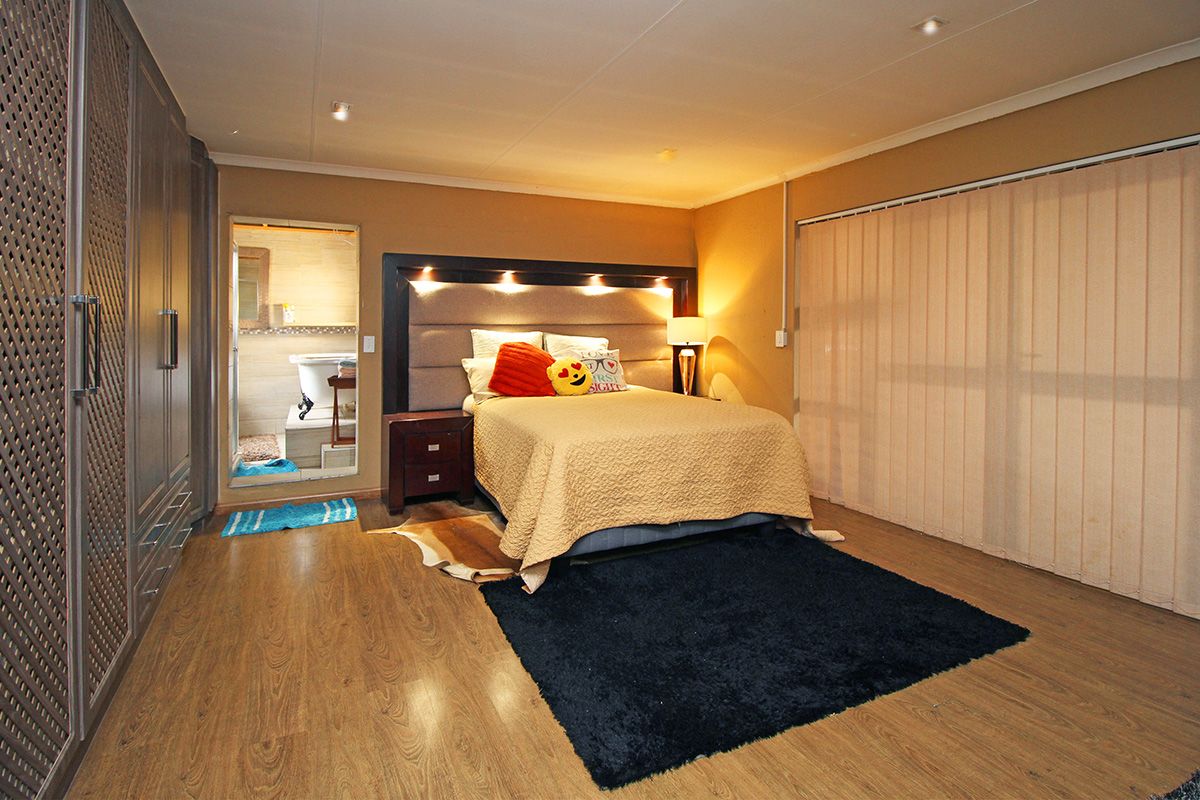 Spacious bedroom featuring built-in cabinetry, integrated headboard lighting, laminate flooring, and direct access to an en-suite bathroom.