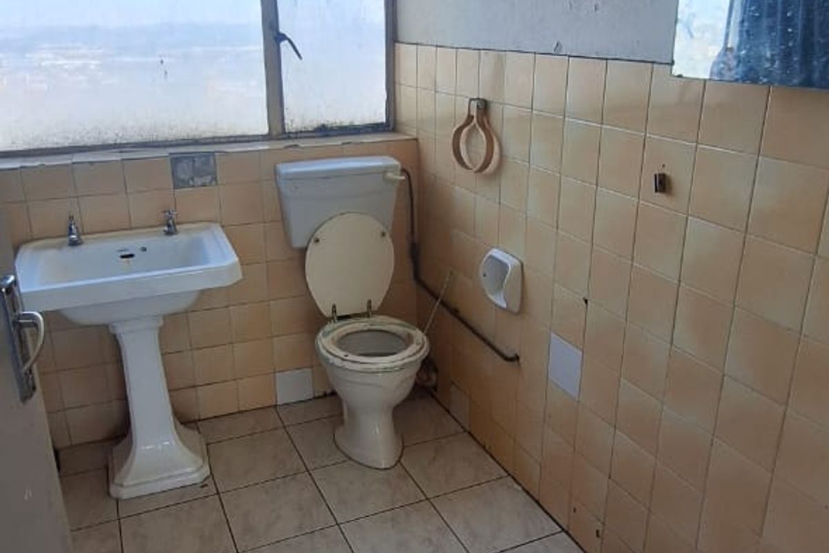 A dated bathroom featuring a pedestal basin, toilet, and tiled walls. The space requires renovation to update the finishes and fixtures.
