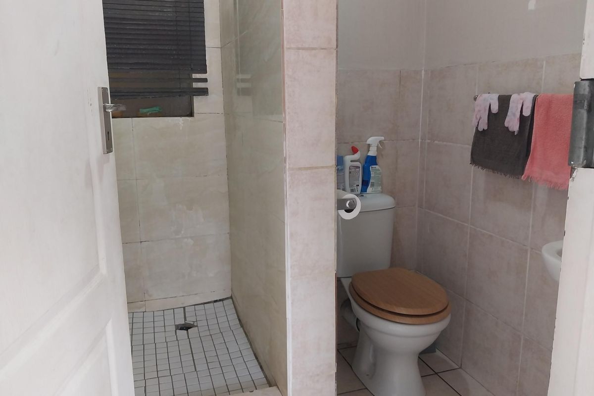 A functional bathroom featuring a tiled shower enclosure, a standard toilet, and neutral wall tiling throughout.