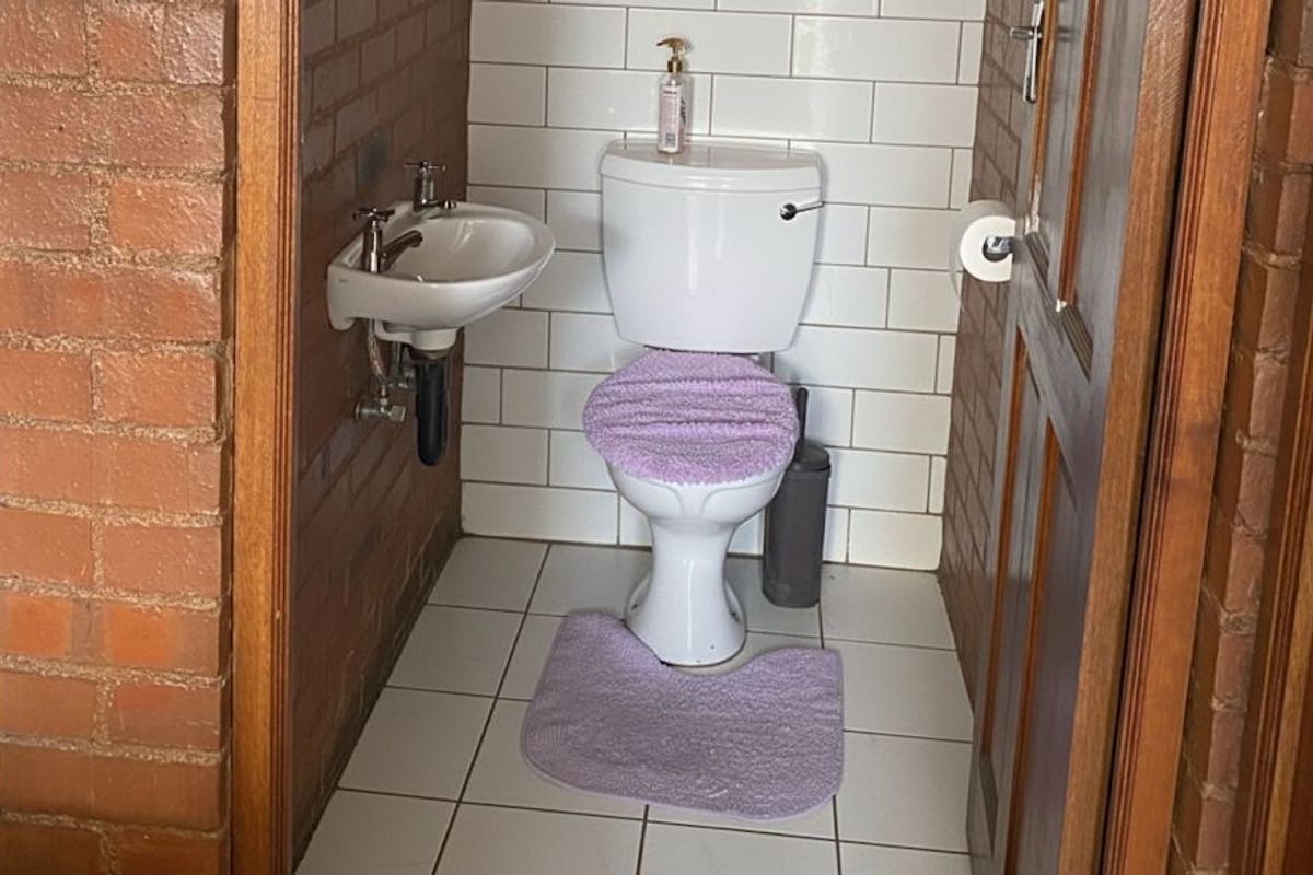 A compact guest bathroom featuring a white toilet, wall-mounted basin, white subway tile backsplash, and exposed brick walls.