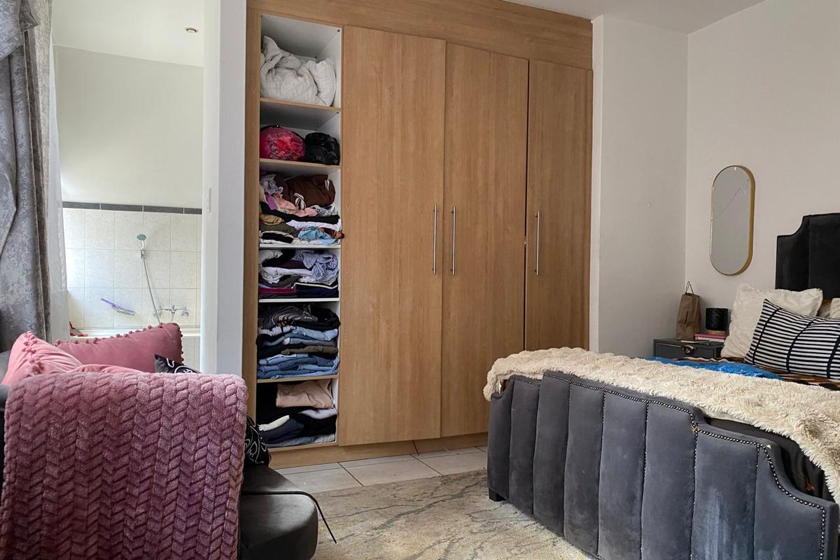 A bedroom featuring built-in light wood-grain wardrobes with integrated shelving and recessed ceiling lighting, with an adjacent view into a tiled bathroom area.