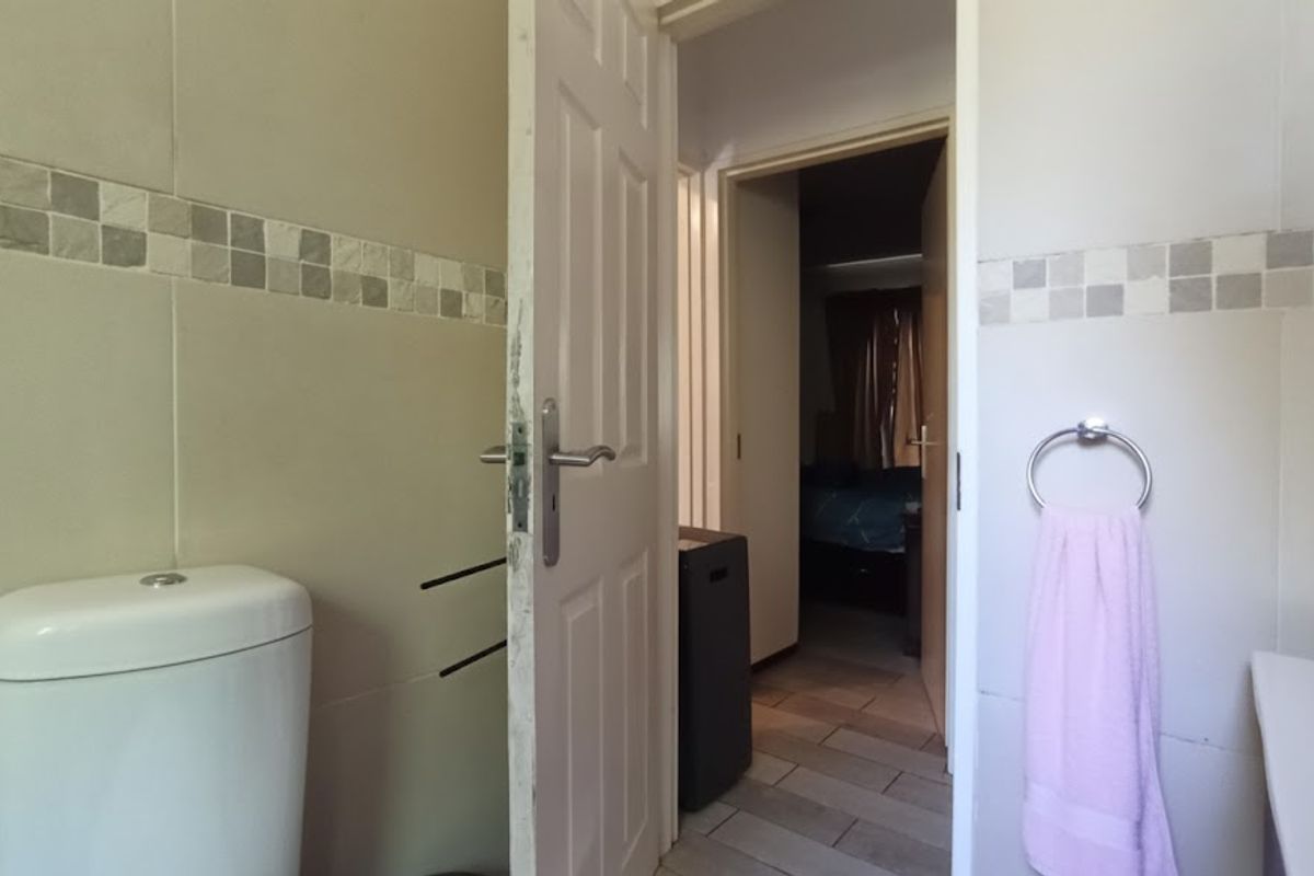 A functional bathroom featuring tiled walls with a decorative mosaic border, a standard toilet, and a doorway leading into an adjacent bedroom.
