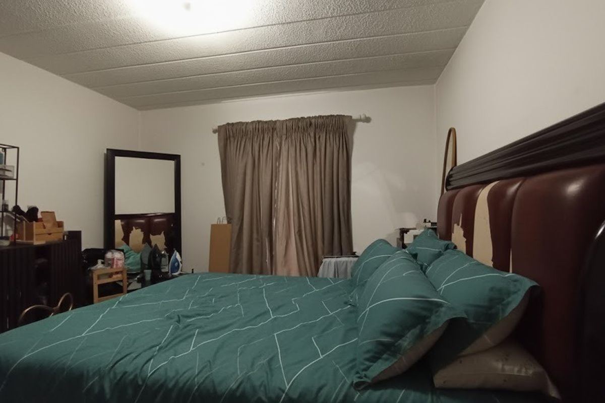 A bedroom featuring a textured ceiling and a window dressed with curtains.