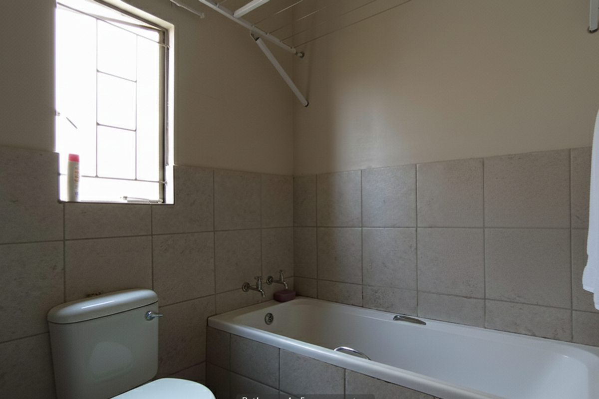 A functional bathroom featuring a built-in bathtub, wall-mounted taps, a toilet, and a window with security bars.