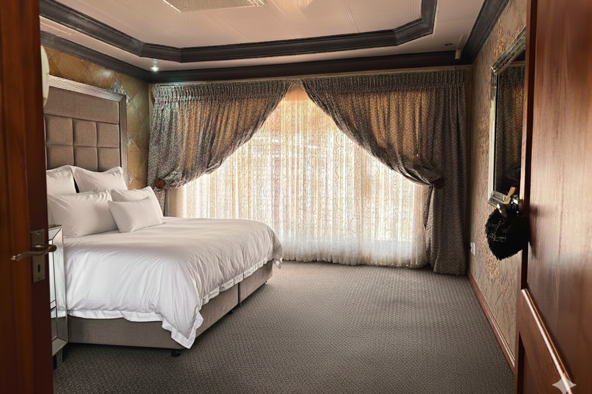 Spacious bedroom featuring a tray ceiling, carpeted flooring, and large windows with draped curtains.