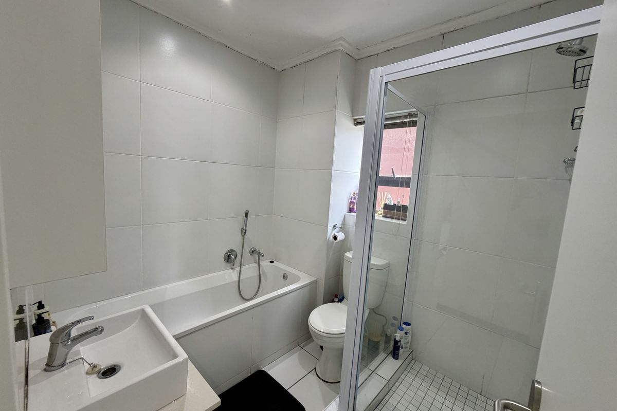 A functional bathroom featuring a white bathtub, separate glass-enclosed shower, vanity basin, and toilet with neutral wall tiling.
