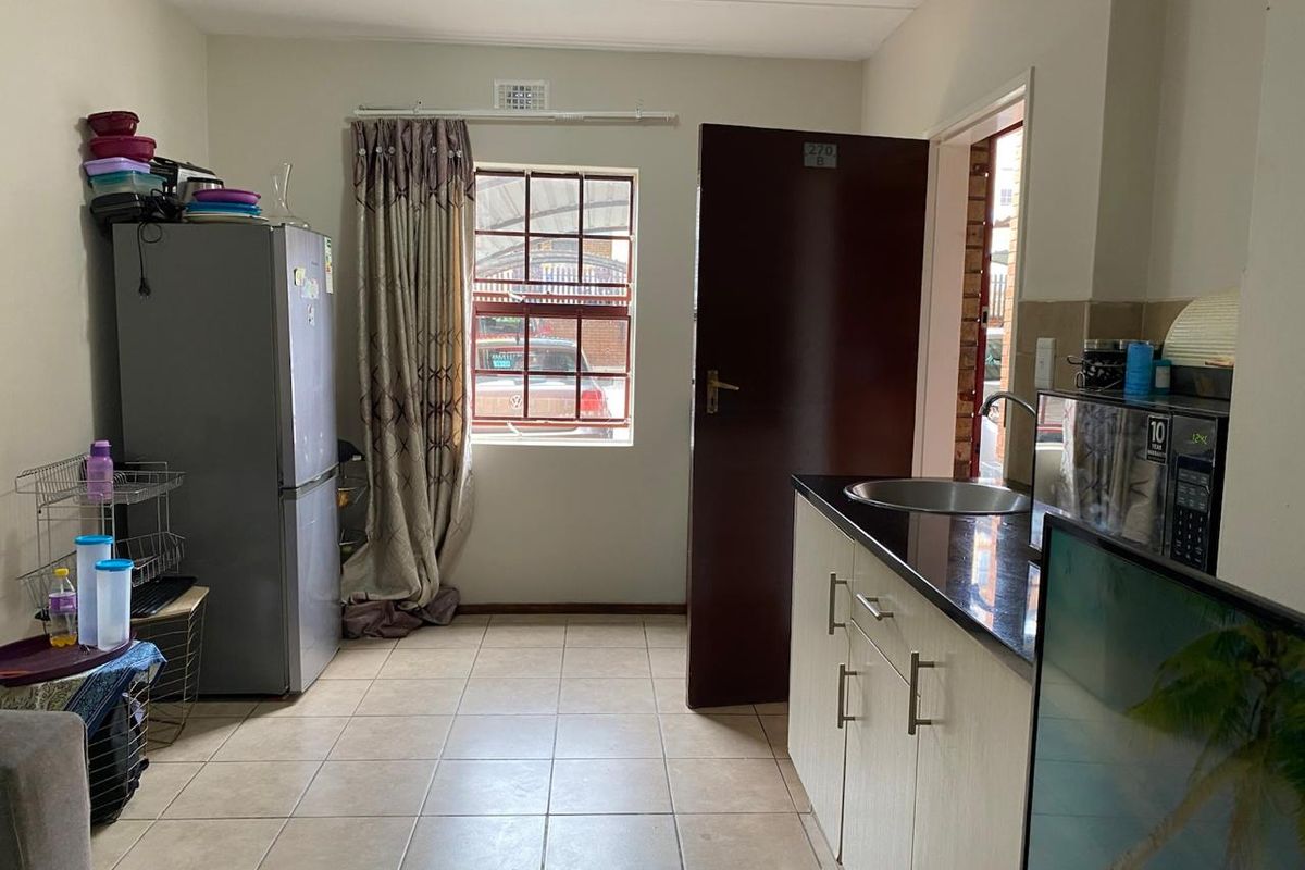 A functional kitchen area featuring tiled flooring, built-in cabinetry with dark countertops, a stainless steel sink, and a window providing natural light.