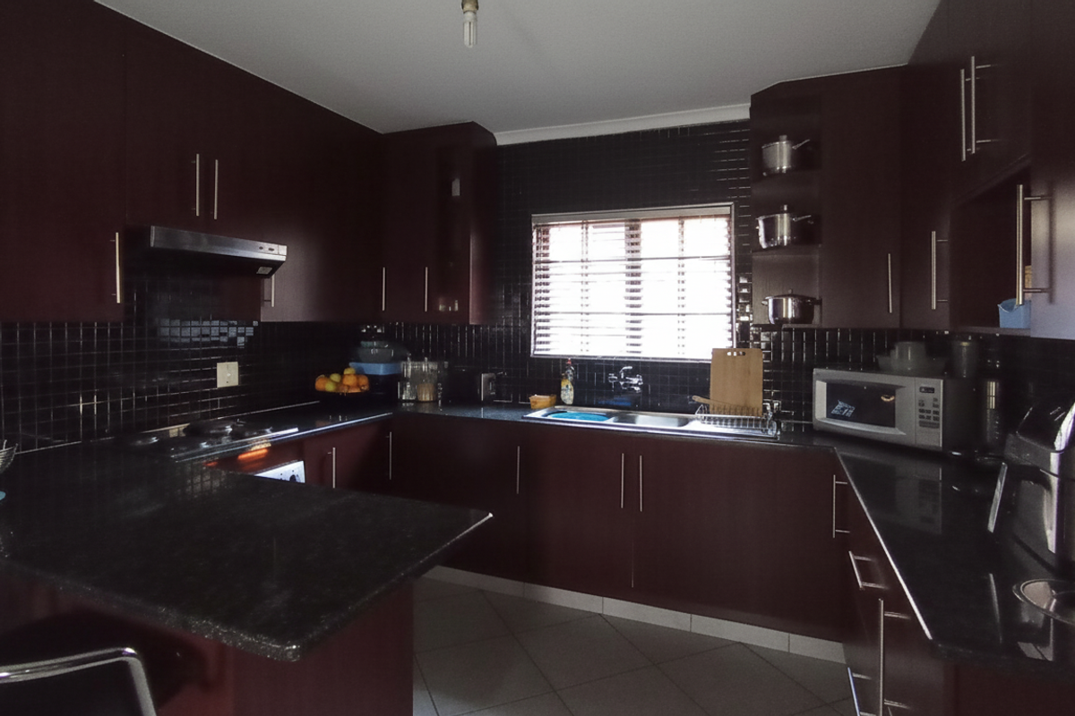 A functional kitchen featuring dark cabinetry, granite countertops, a built-in hob, extractor fan, and a double sink with tiled splashbacks.