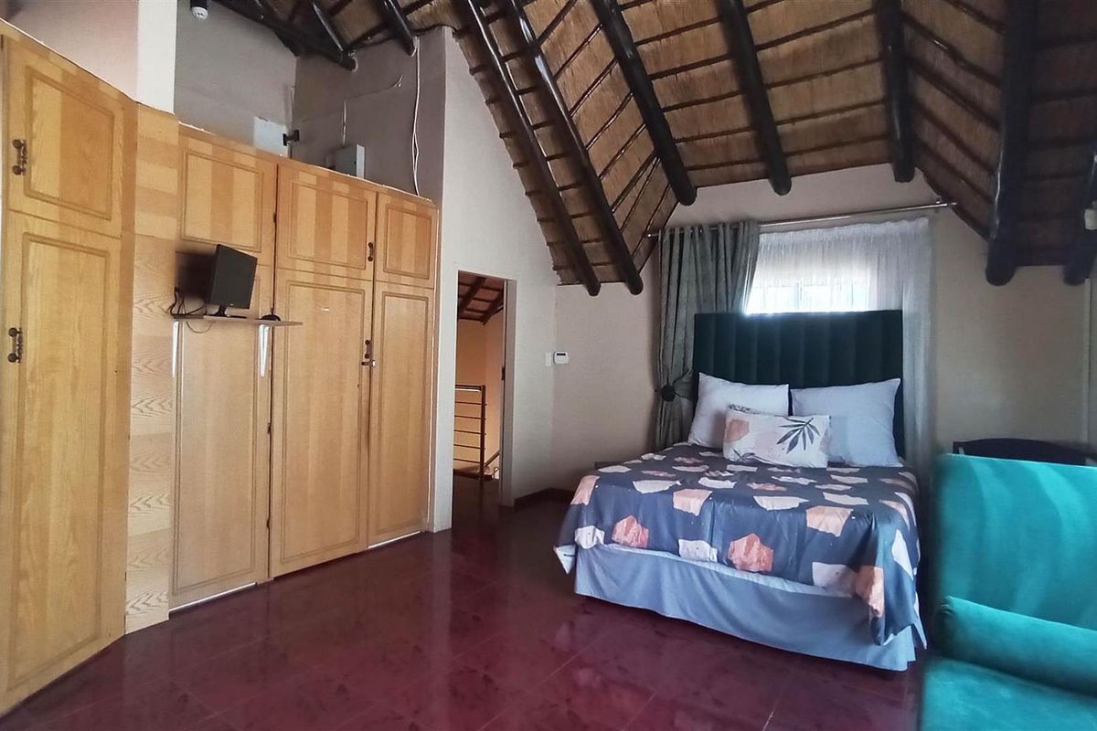 Spacious bedroom featuring a high vaulted thatched ceiling with exposed timber beams and extensive built-in wooden cabinetry.