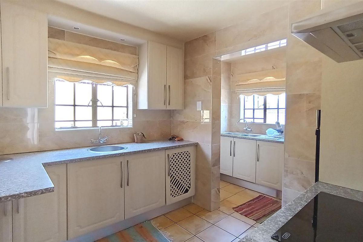A well-maintained kitchen featuring stone-look wall tiling, ample cabinetry, a built-in hob, and an extractor fan, with an adjoining scullery area.