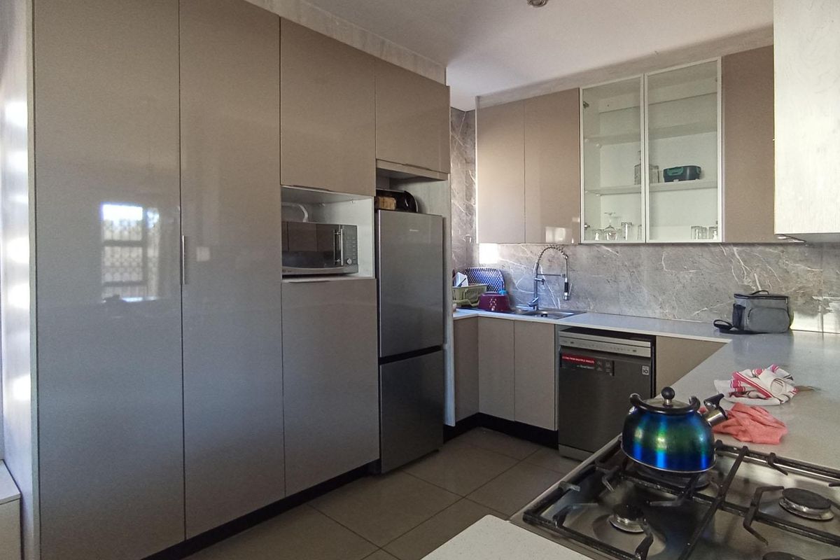 Modern kitchen featuring high-gloss cabinetry, stone-look splashbacks, integrated microwave housing, stainless steel sink, and a built-in gas hob.