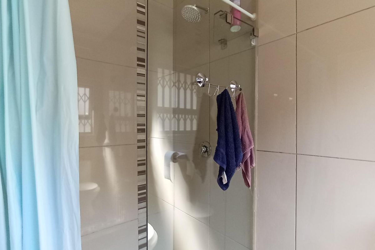 A functional bathroom shower area featuring tiled walls, a glass shower screen, and a wall-mounted shower head.
