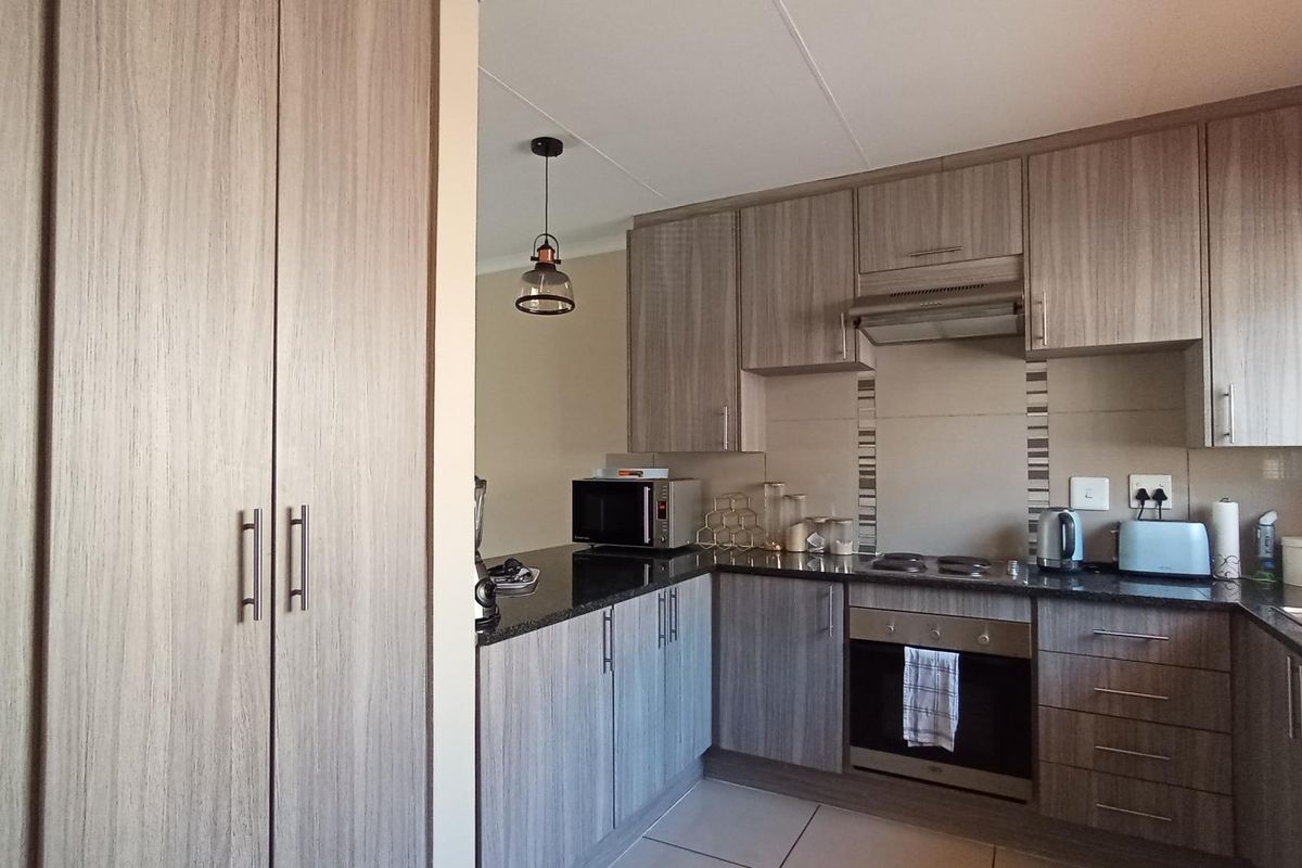 Modern kitchen featuring wood-grain cabinetry, granite countertops, built-in oven, extractor fan, and tiled flooring.