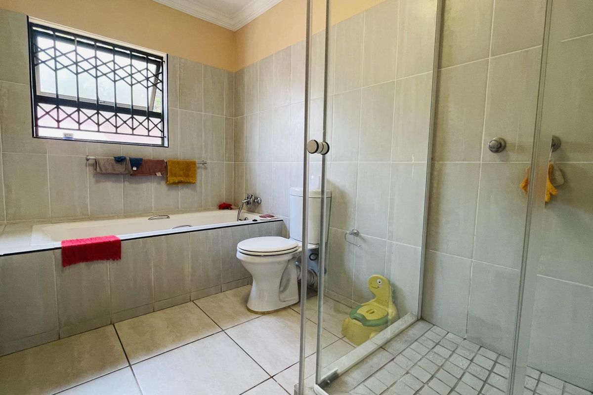 A functional bathroom featuring a built-in bathtub, separate glass-enclosed shower, toilet, and neutral wall and floor tiling.