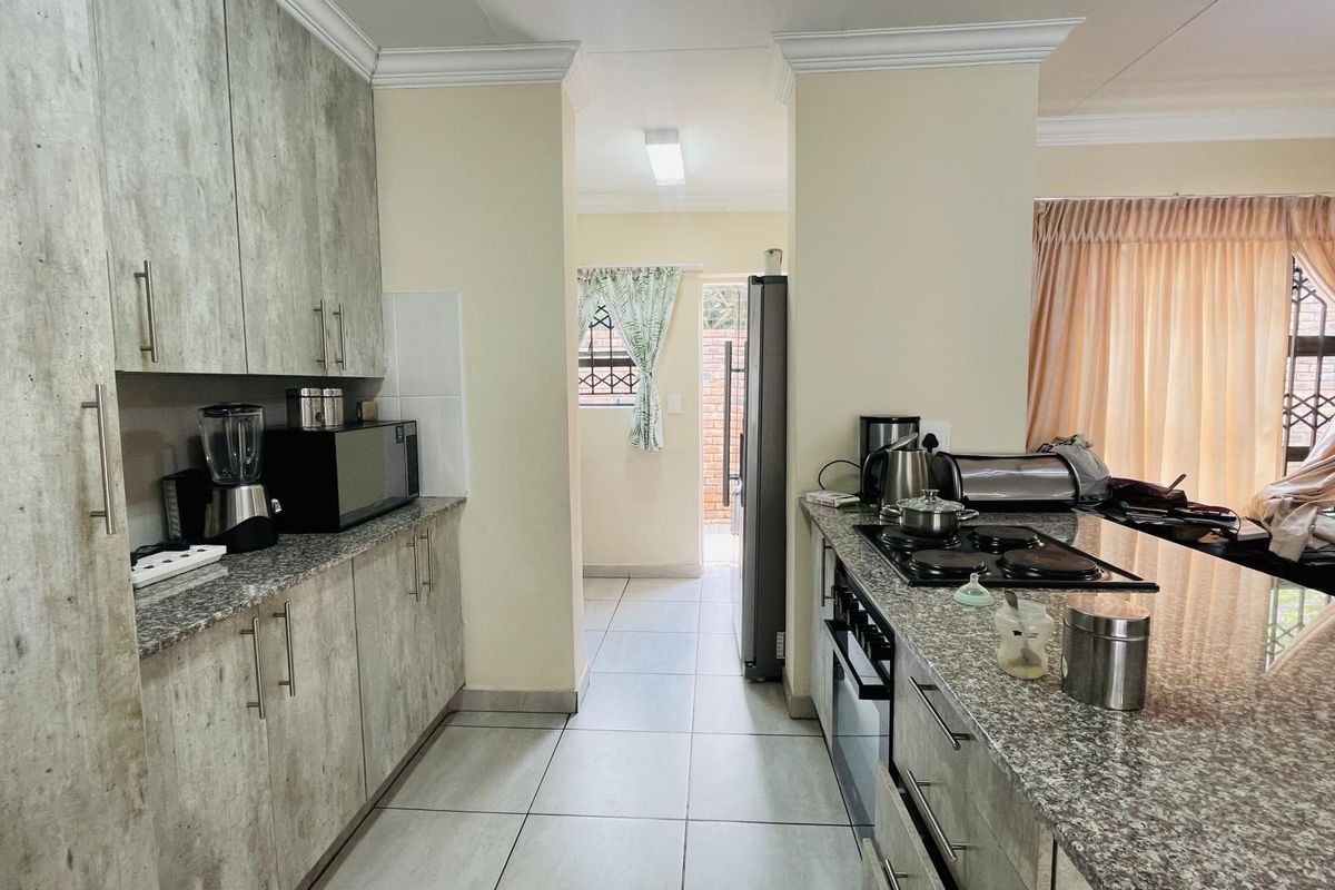 Modern kitchen featuring granite countertops, built-in cabinetry, and a fitted hob and oven, leading to a functional scullery area.
