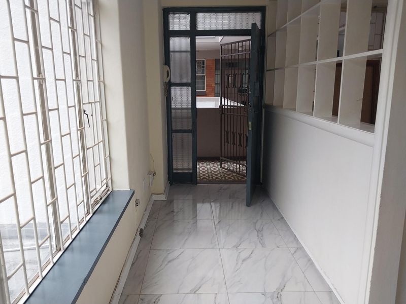An entrance area featuring marble-look tiled flooring, built-in shelving, and a security gate leading to the exterior.