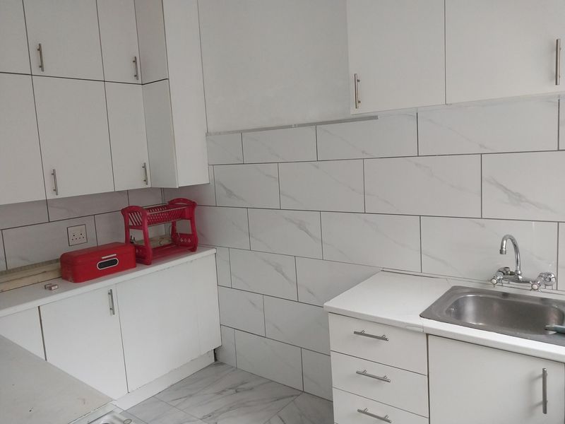 A clean, modern kitchen featuring white cabinetry, marble-look wall and floor tiles, and a stainless steel sink with a chrome mixer tap.